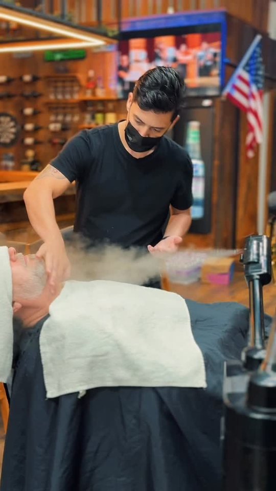 Barbeiro aplicando toalha quente em cliente na The Barber Pub